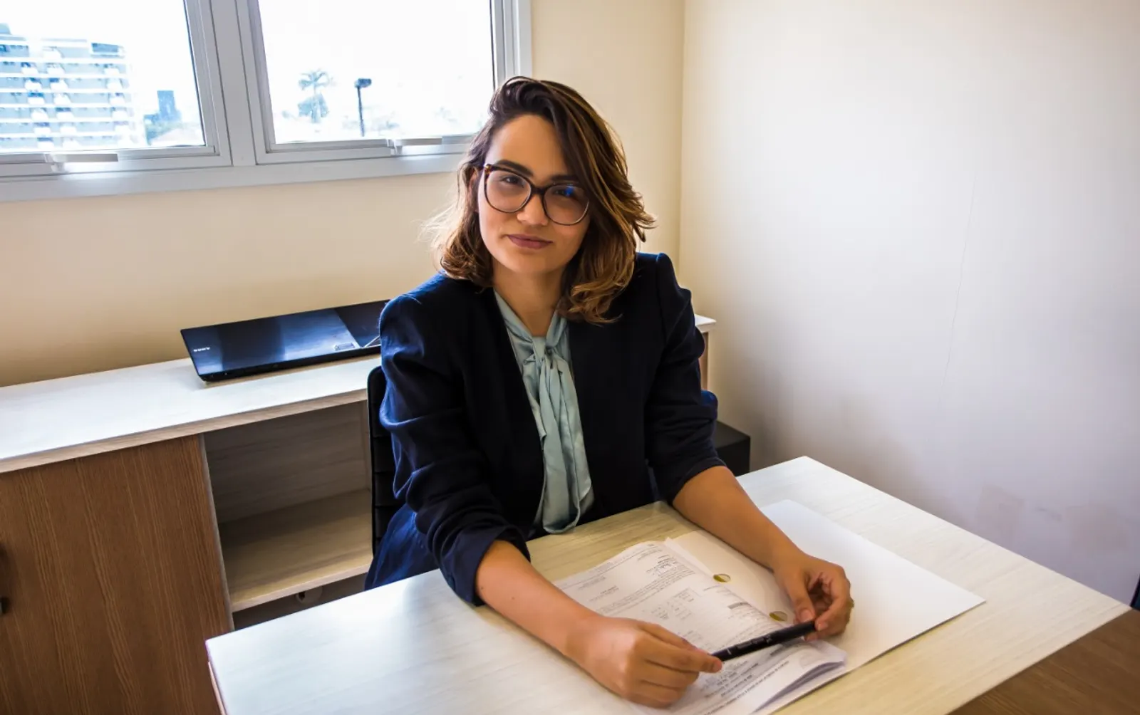 Bárbara Massoni analisando documentos em sua mesa de trabalho